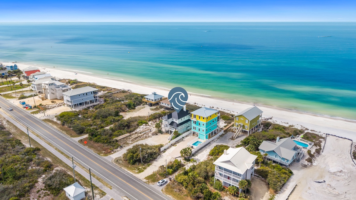 Stunning aerial view of beachfront vacation homes along pristine white sand beach with crystal-clear turquoise waters stretching to the horizon.