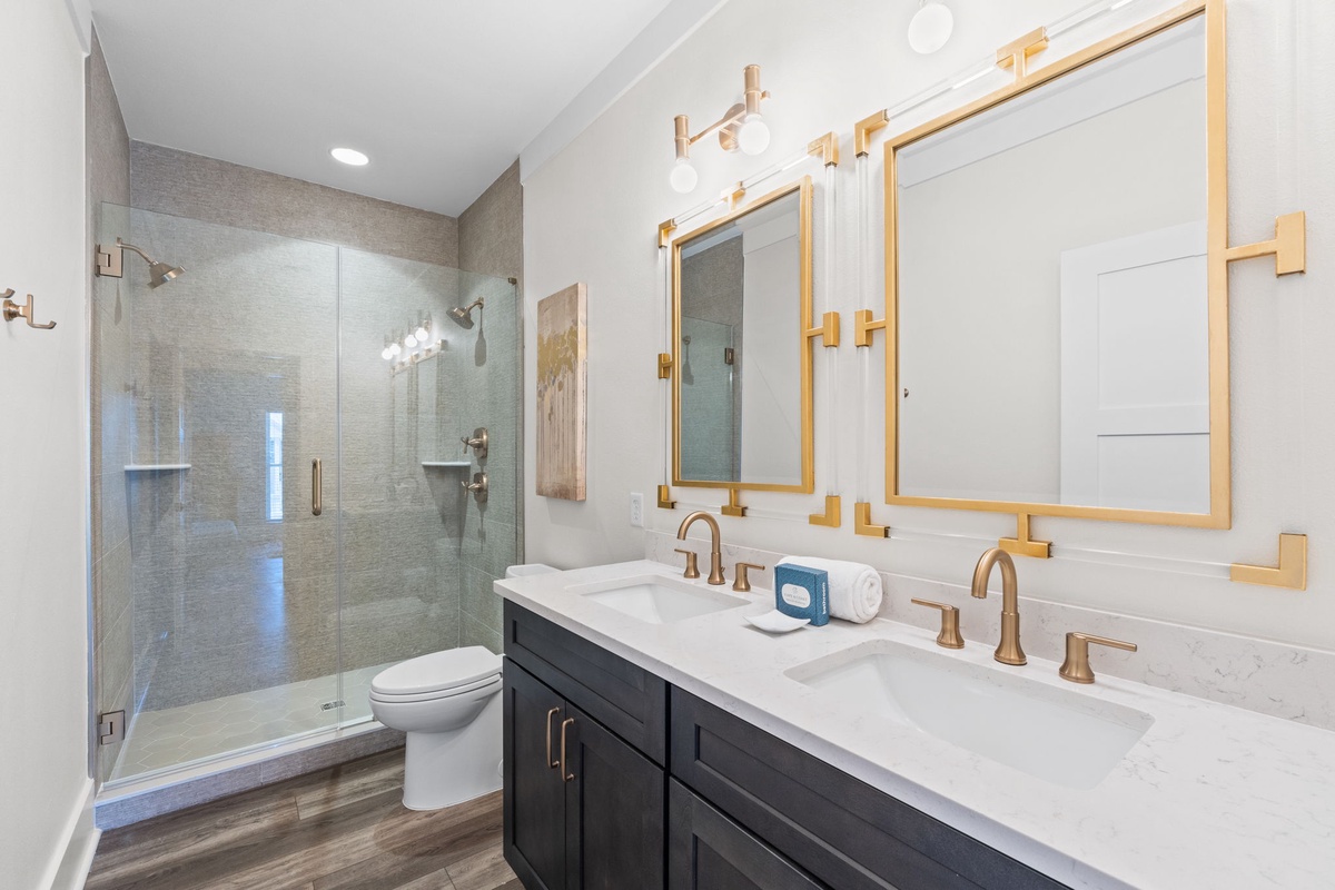 Your spacious bathroom awaits with dual vanities, elegant gold fixtures, and a beautifully tiled walk-in shower for refreshing mornings.