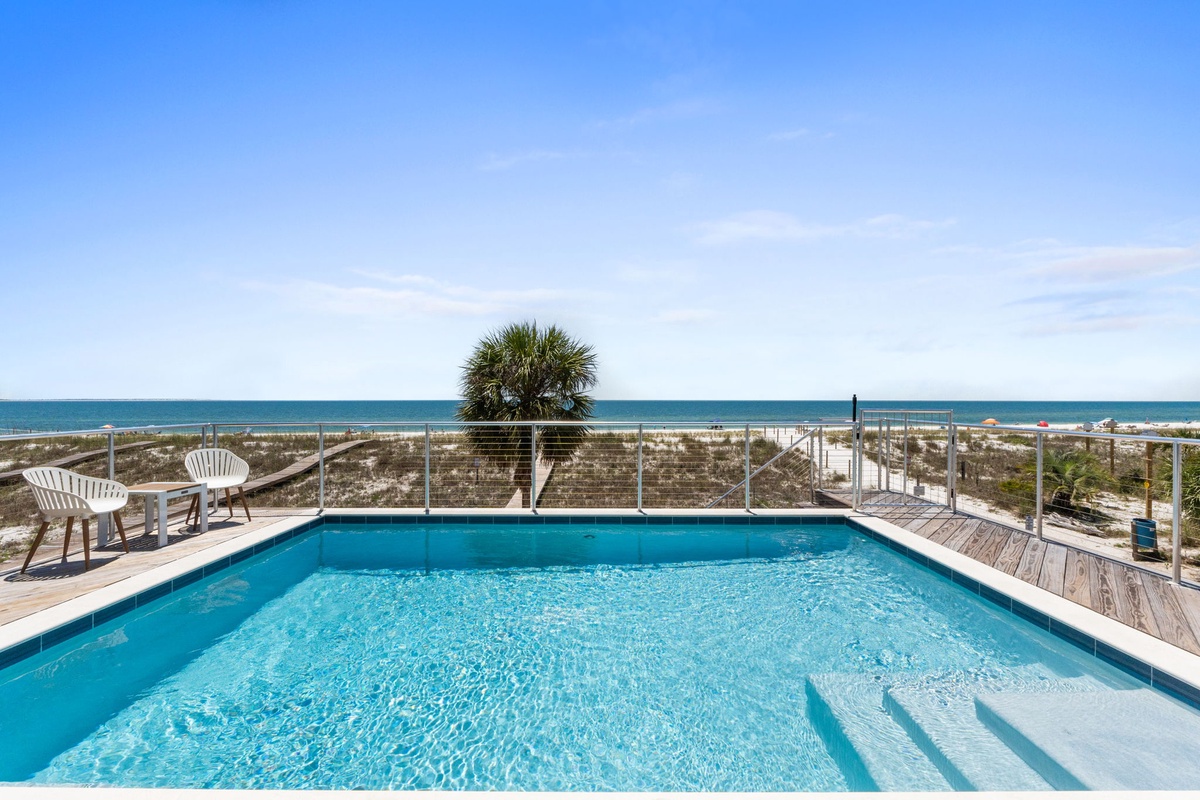 Crystal-clear waters meet soft sandy shores just beyond the sparkling pool, where you can lounge under sunny skies with breathtaking coastal views stretching across the horizon.