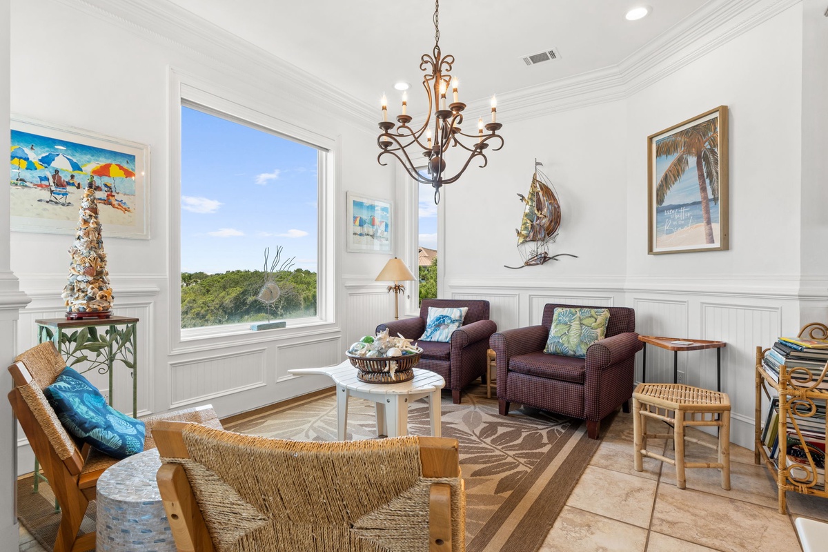 Relax in this bright, coastal-inspired living room where natural light pours through large windows framing lush greenery. Sink into comfortable seating, enjoy beach-themed art, and feel the vacation vibes all around you.