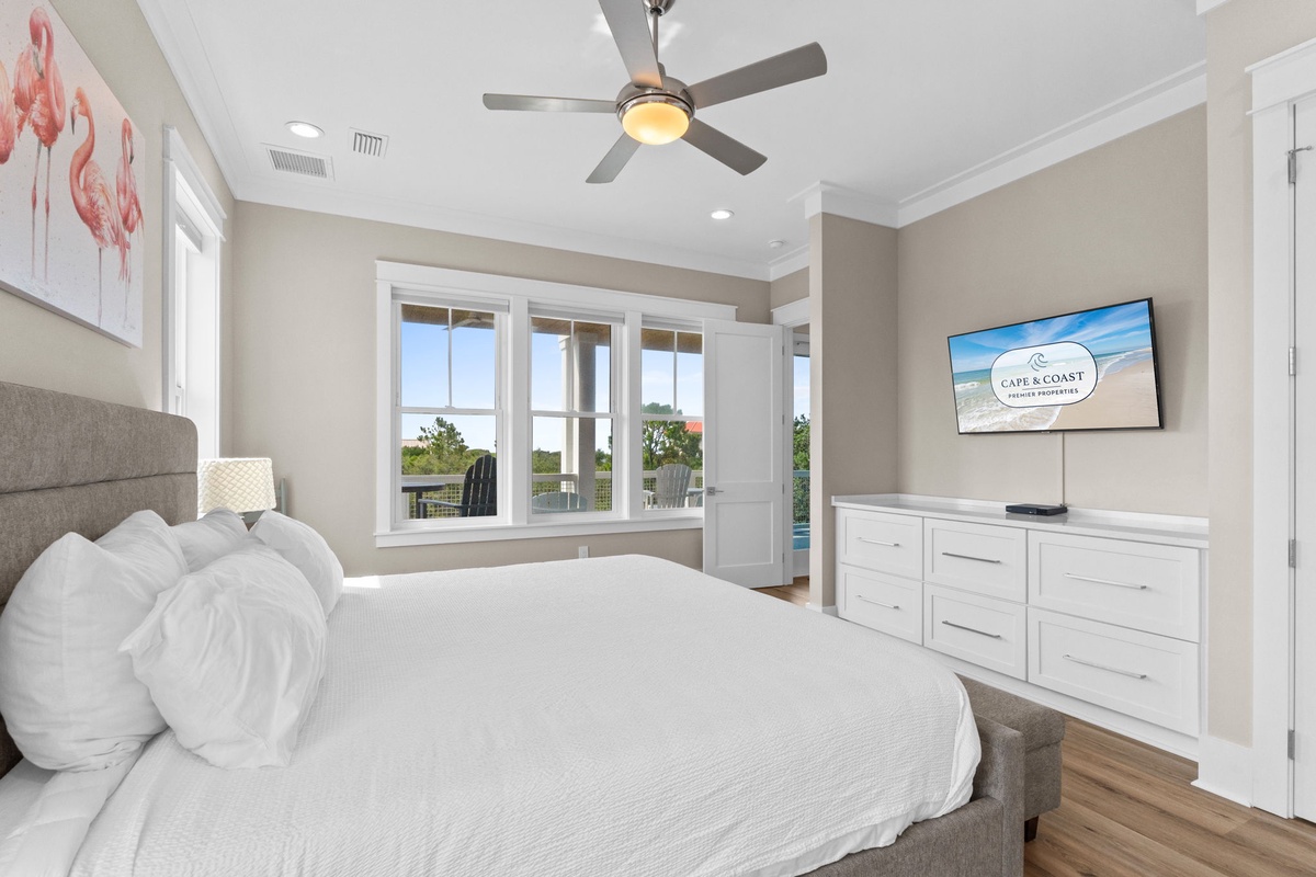 Sink into your plush bed where soft linens and a gentle ceiling fan promise restful nights. Natural light spills through glass doors leading to your private balcony, inviting you to unwind in comfort.