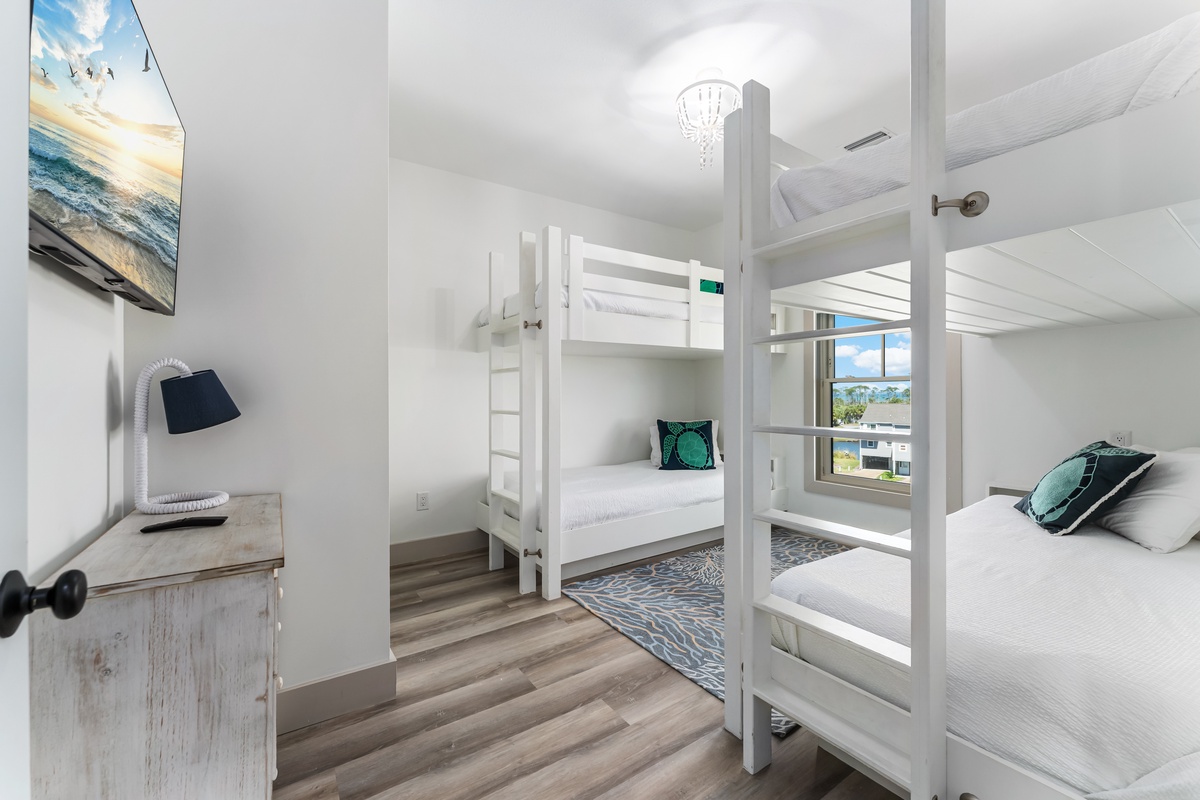 Your spacious bedroom features bunk beds and a queen bed, perfect for family gatherings with ocean artwork and natural light streaming in.