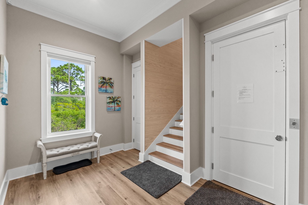 Step inside to a bright, welcoming entryway with natural light streaming through the window, warm wood floors beneath your feet, and a cozy bench where you can settle in and feel instantly at home.