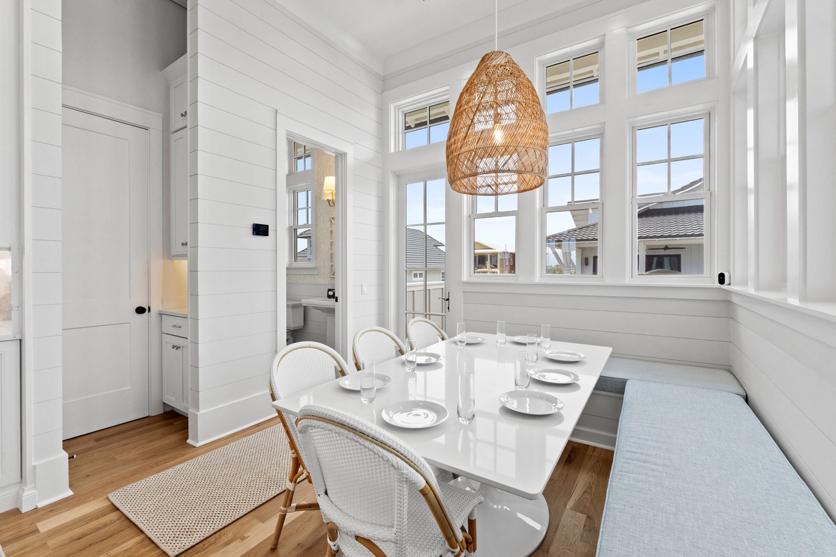 Light-filled dining nook features coastal charm with shiplap walls, cozy banquette seating, and a woven pendant that casts warm, inviting light for your meals together.