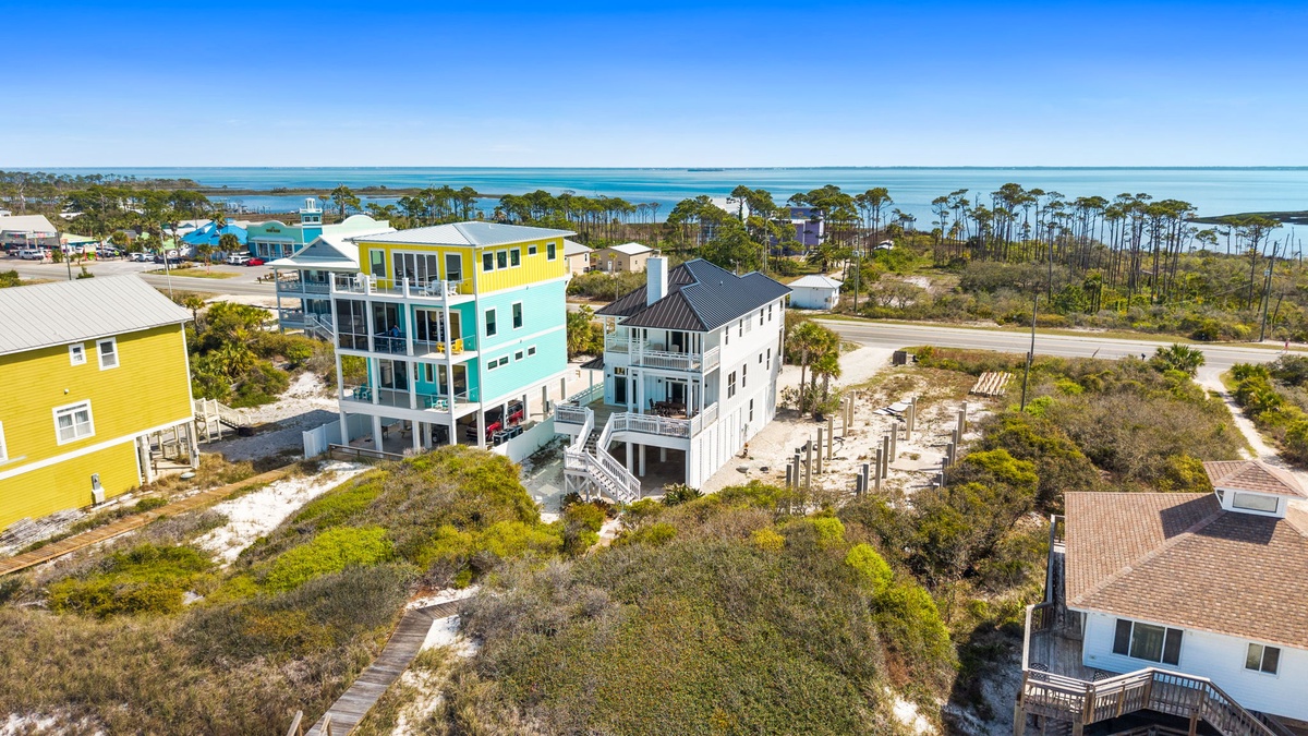 Colorful beachfront homes nestled among coastal dunes with pristine waters and natural vegetation creating a serene coastal community setting.