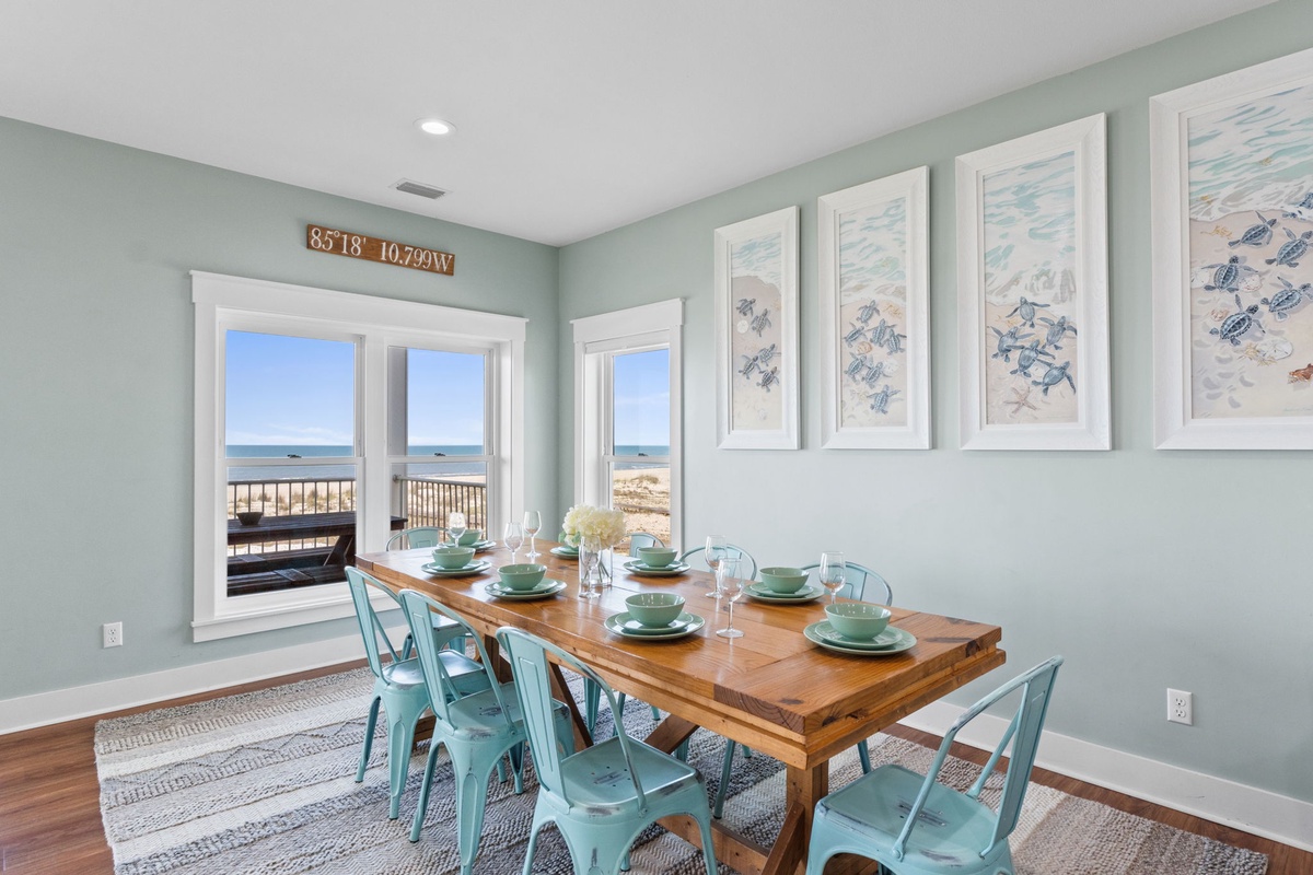 Gather around this coastal dining table with turquoise chairs and sea turtle artwork as ocean views stretch through large windows, creating your perfect beachside meal setting.