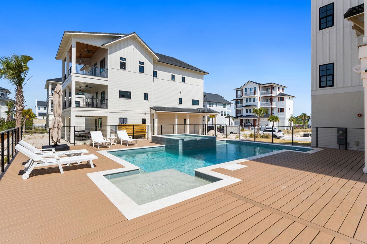 Modern beach home featuring a sparkling pool and spa on an elevated deck, surrounded by contemporary coastal architecture under clear blue skies.