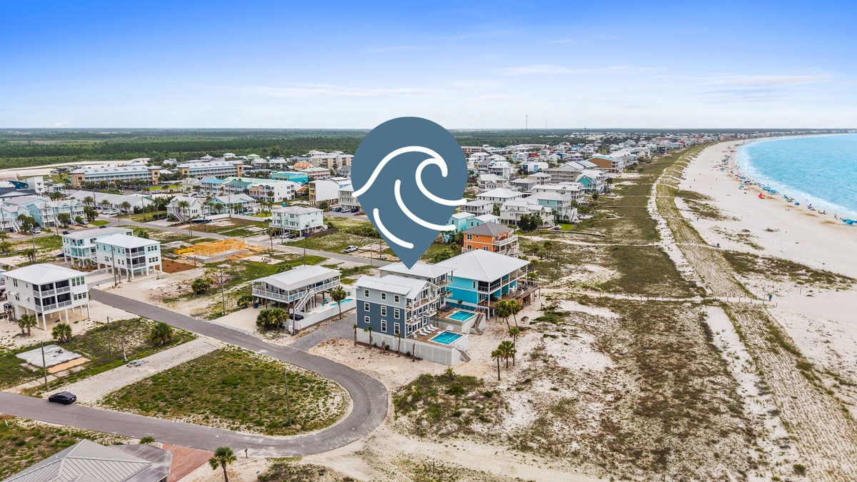 Aerial view of a beachfront vacation rental community nestled between the turquoise gulf waters and coastal residential area, showcasing the property's prime location along white sandy shores.