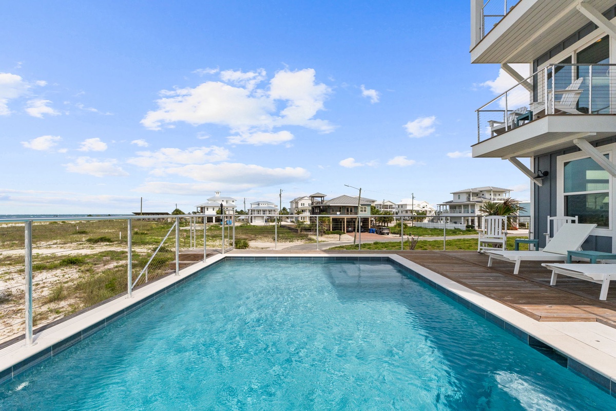 A sparkling pool surrounded by sunny decking and coastal breezes. The property sits in a peaceful beachside neighborhood with water views in the distance.