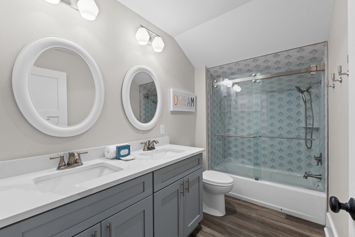 Bright, modern bathroom with dual sinks and a stylish glass-enclosed tub—perfect for your morning routine and unwinding after a day of adventure.