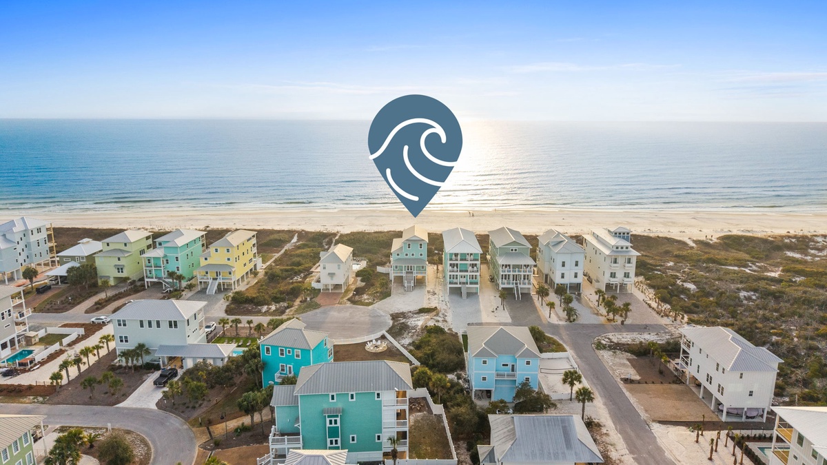 Aerial view of colorful beachfront vacation homes nestled between coastal dunes and pristine shoreline during golden hour.