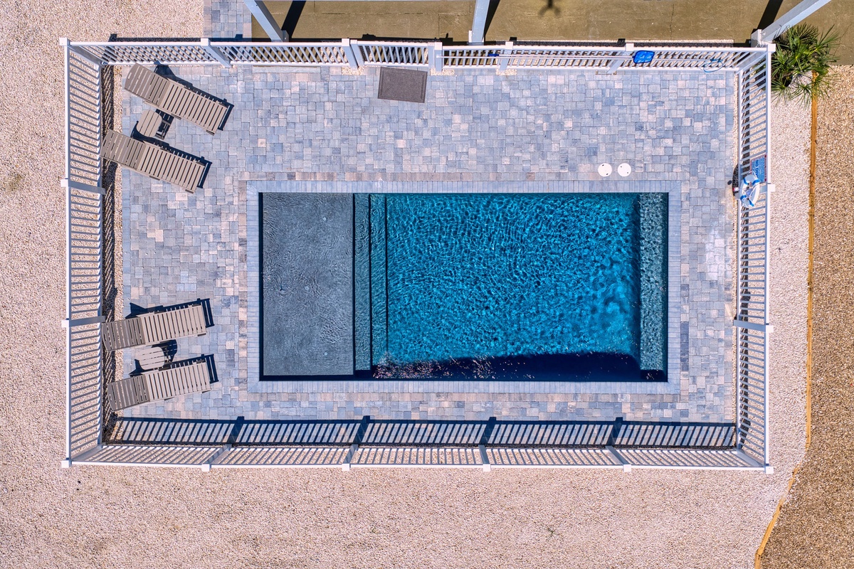 An aerial view reveals the property's sparkling pool surrounded by Mediterranean-style tile work, sun loungers, and beachside surroundings—offering a serene coastal retreat setting.