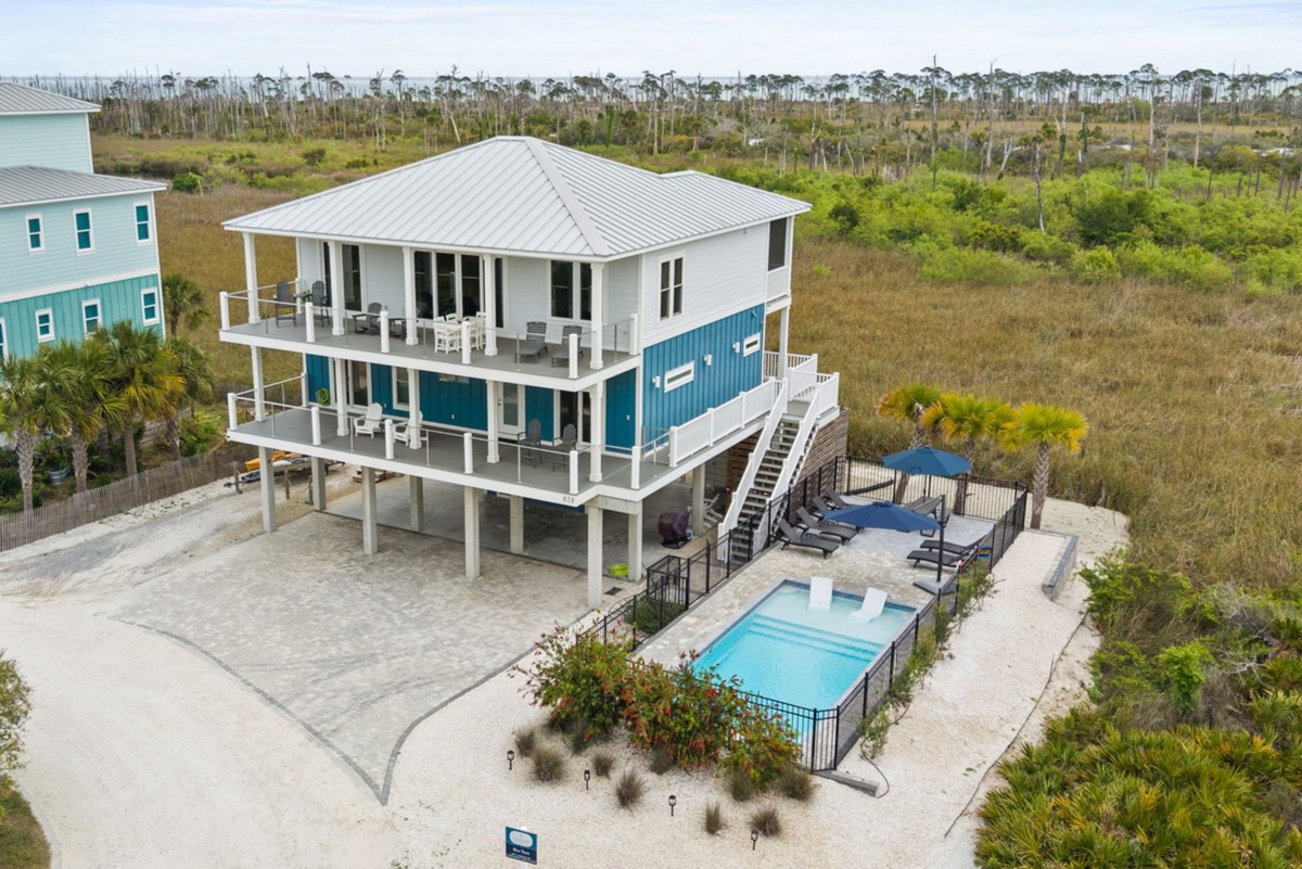 Aerial view of a modern coastal vacation home featuring multiple levels, wraparound balconies, and a private pool surrounded by natural wetland preserve.