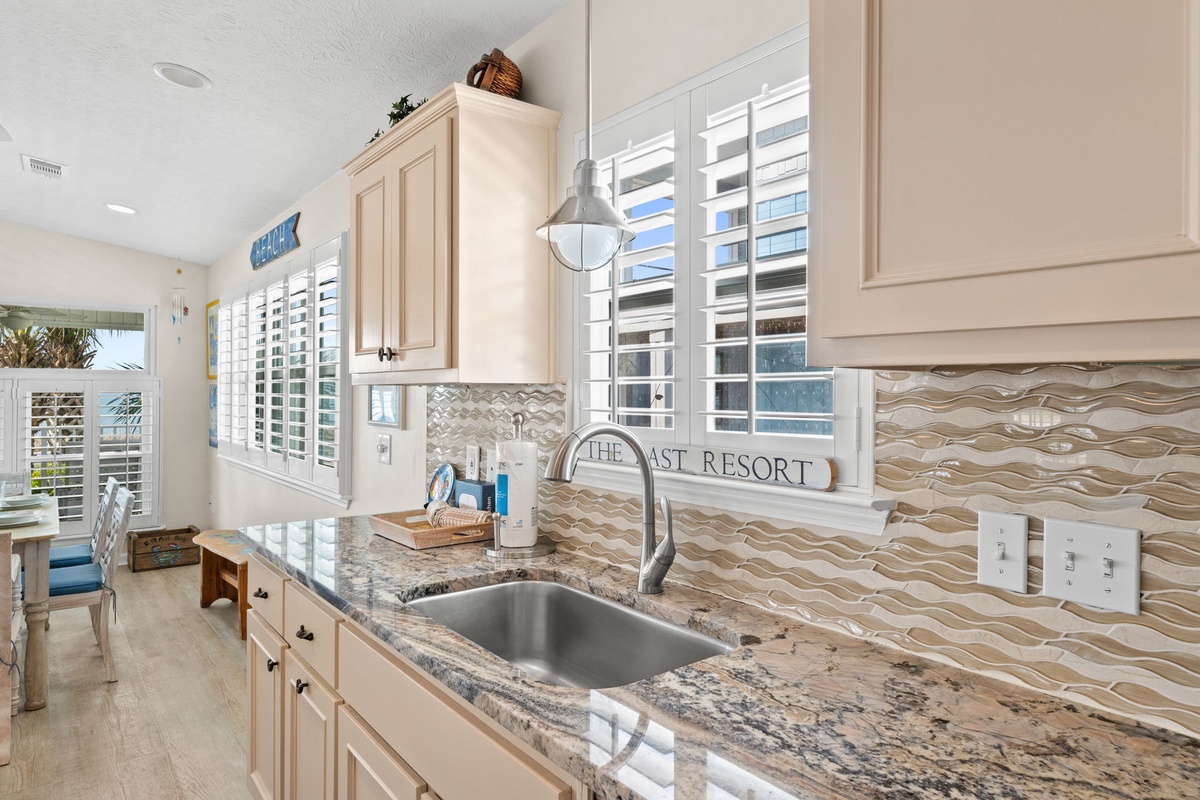 Your coastal kitchen awaits with granite counters, wave-patterned backsplash, and shuttered windows flooding the space with natural light.