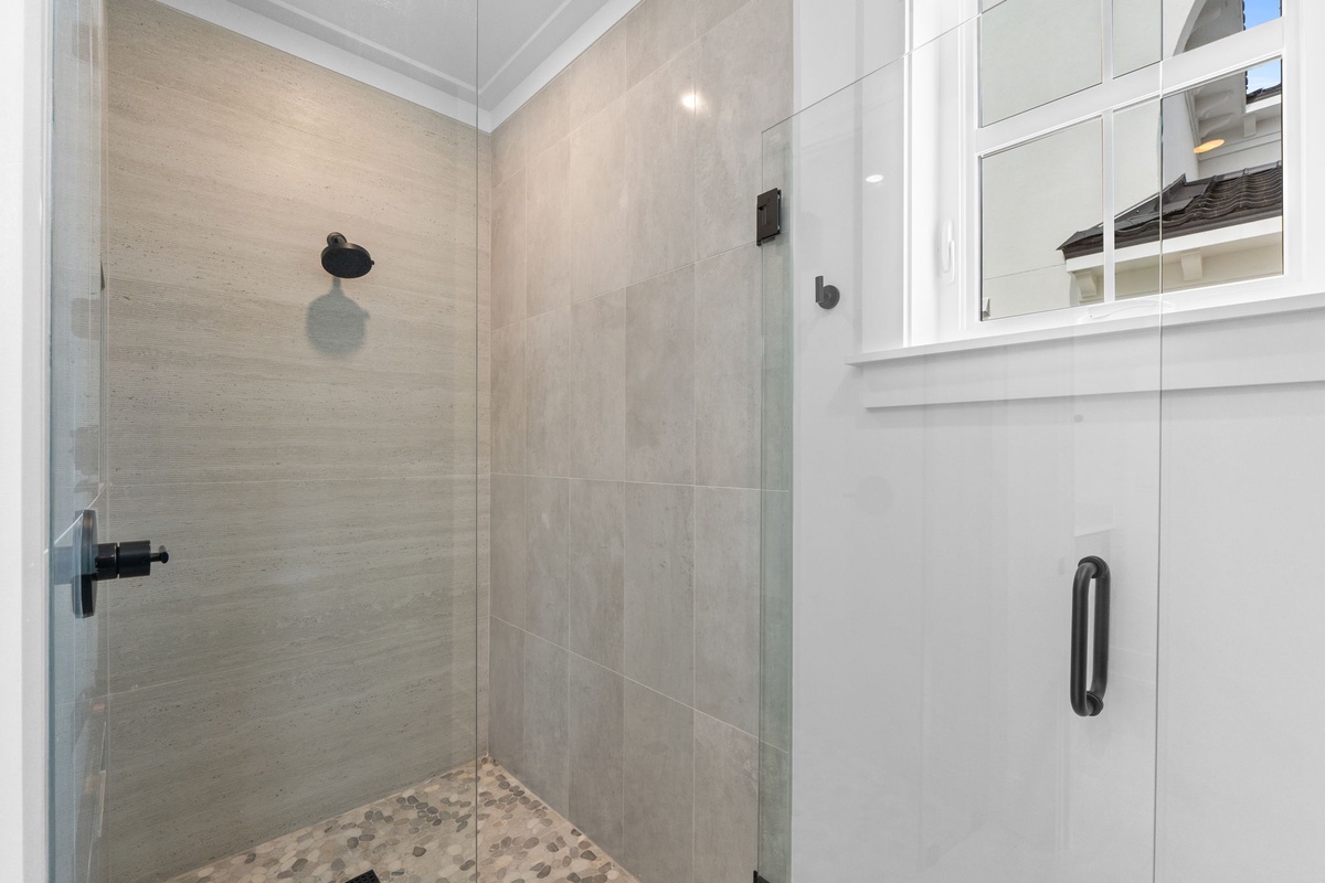 Step into your private walk-in shower featuring elegant tile work, a modern black rain showerhead, and pebble stone flooring that massages your feet with every step.