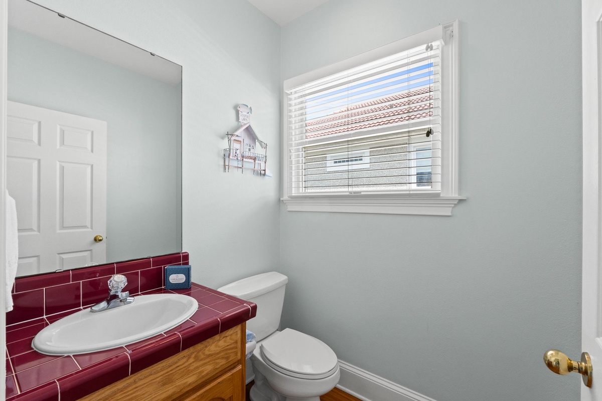 Your private powder room features warm wood vanity and distinctive red tile countertop, with natural light streaming through the window.