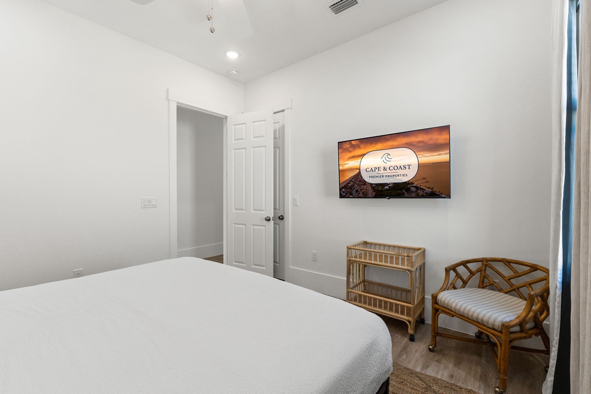 Your peaceful bedroom features crisp white linens and warm touches like the coastal-themed artwork and charming wicker seating area.