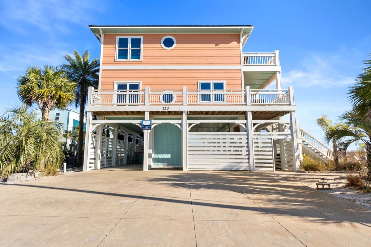 Charming coral-colored beach house on stilts with palm trees and multiple balconies offering coastal comfort.