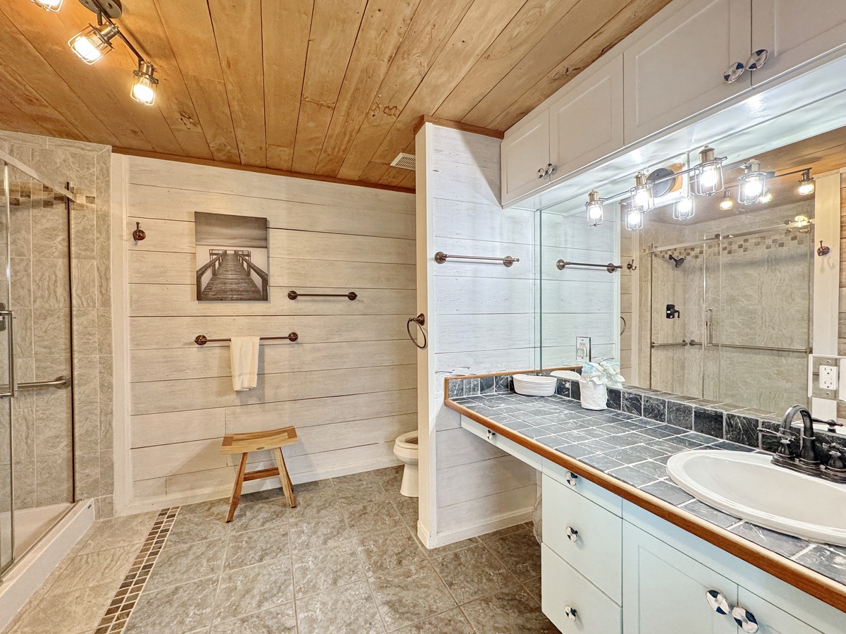 Unwind in your spacious bathroom featuring rustic wood ceiling, modern glass shower, and elegant vanity with thoughtful amenities.
