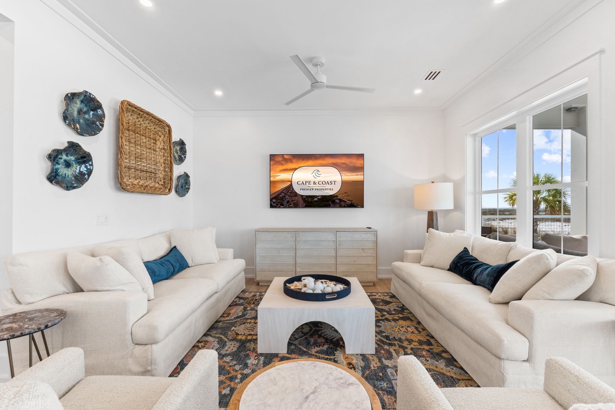 Sink into plush sofas surrounded by coastal artwork and natural light streaming through windows, creating your perfect relaxation haven.