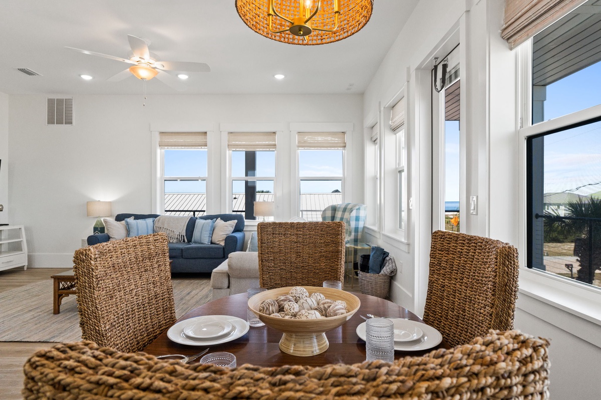 Settle into coastal elegance with wicker dining chairs and ocean views streaming through expansive windows in your bright, airy living space.