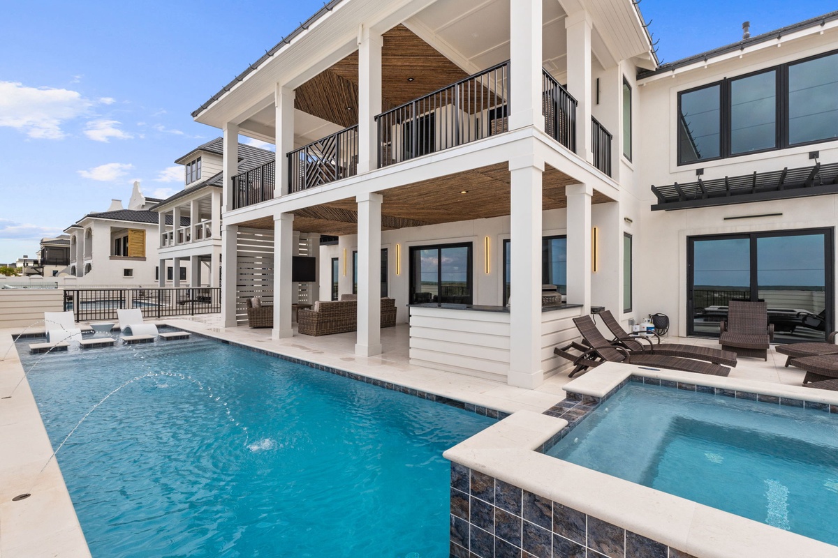 Modern coastal architecture featuring a pristine swimming pool and hot tub, framed by covered terraces and elegant balcony spaces overlooking the beachfront.