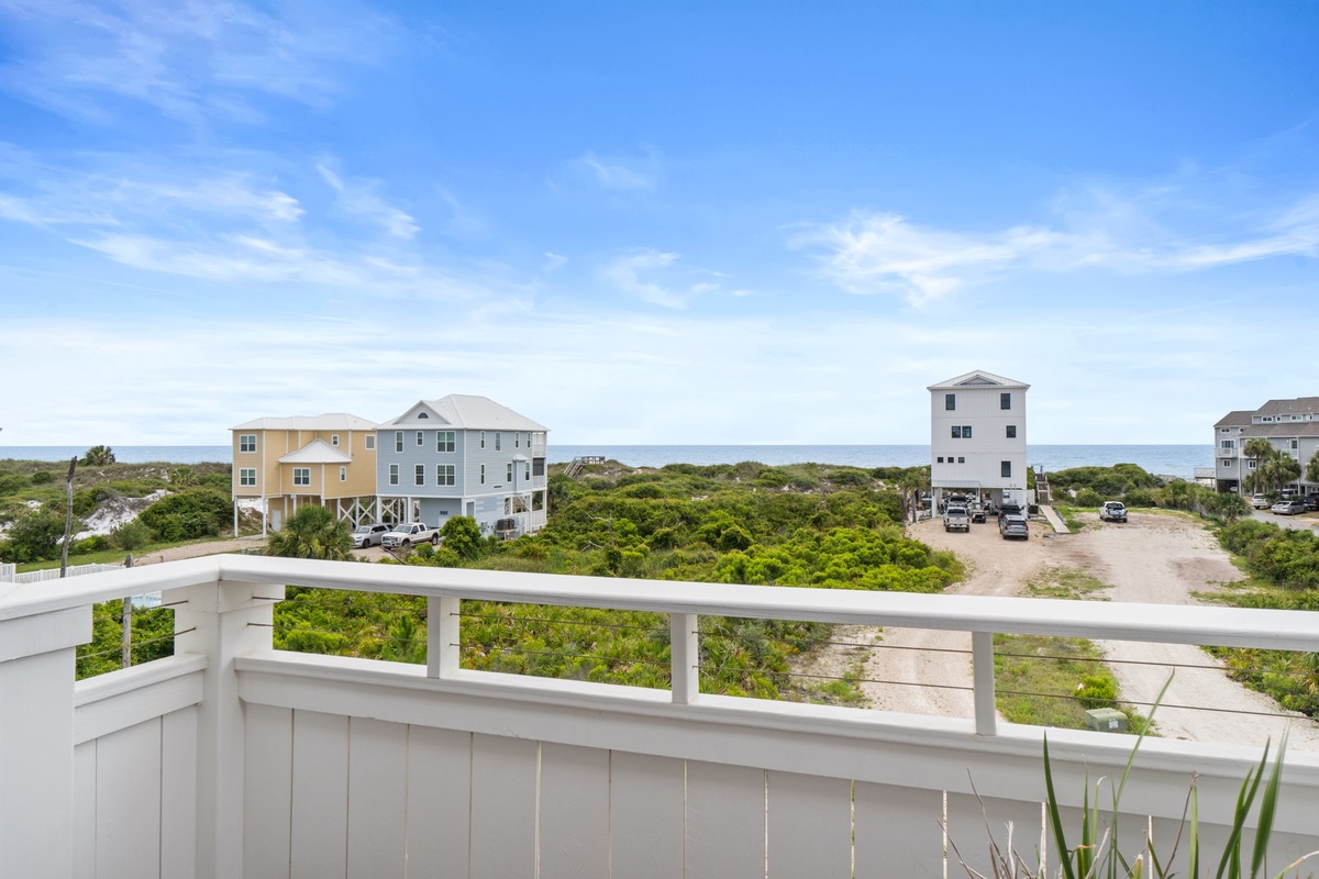 A coastal area surrounded by native vegetation, featuring neighboring beach homes and glimpses of the shoreline beyond.