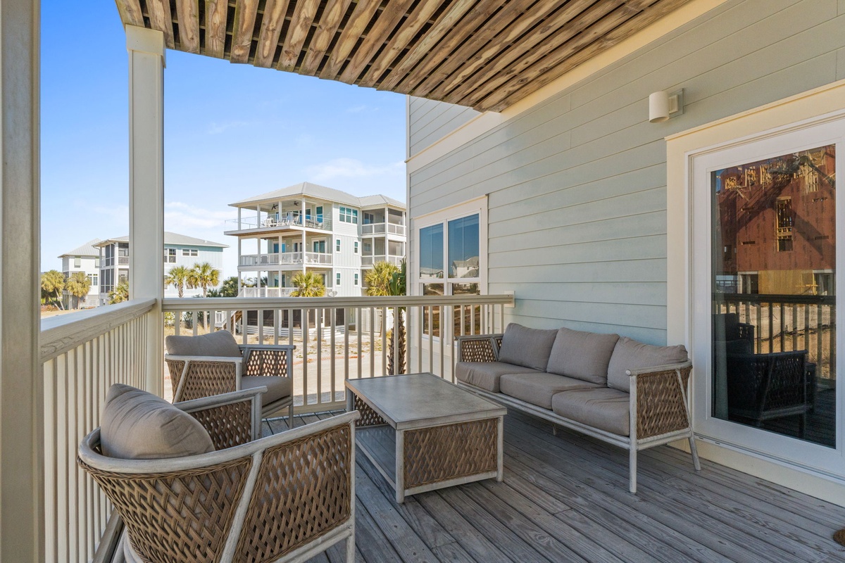 Relax on your private balcony with plush seating, where coastal breezes meet comfortable outdoor living under wood-slat ceiling.