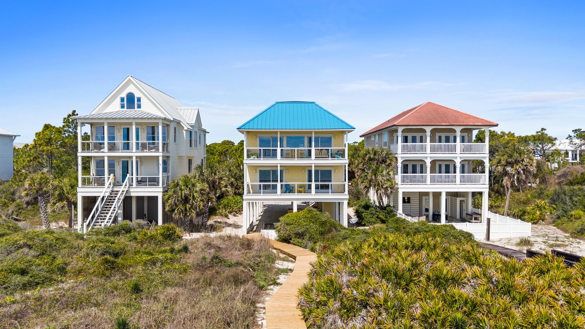 Coastal vacation homes with colorful rooflines nestled among native vegetation and sandy pathways leading to beachfront relaxation.