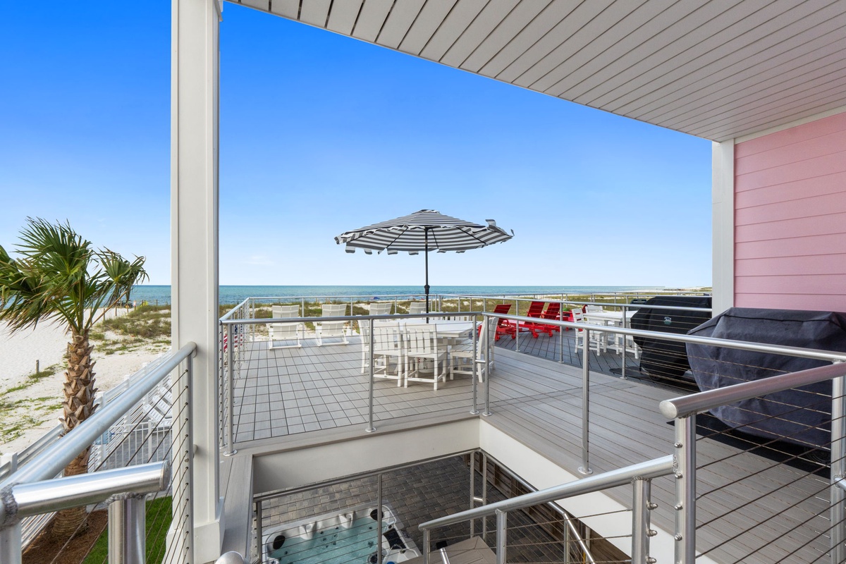 Beachfront deck with ocean views, dining table, striped umbrella, and sandy shores just steps away—perfect for morning coffee or sunset dinners.