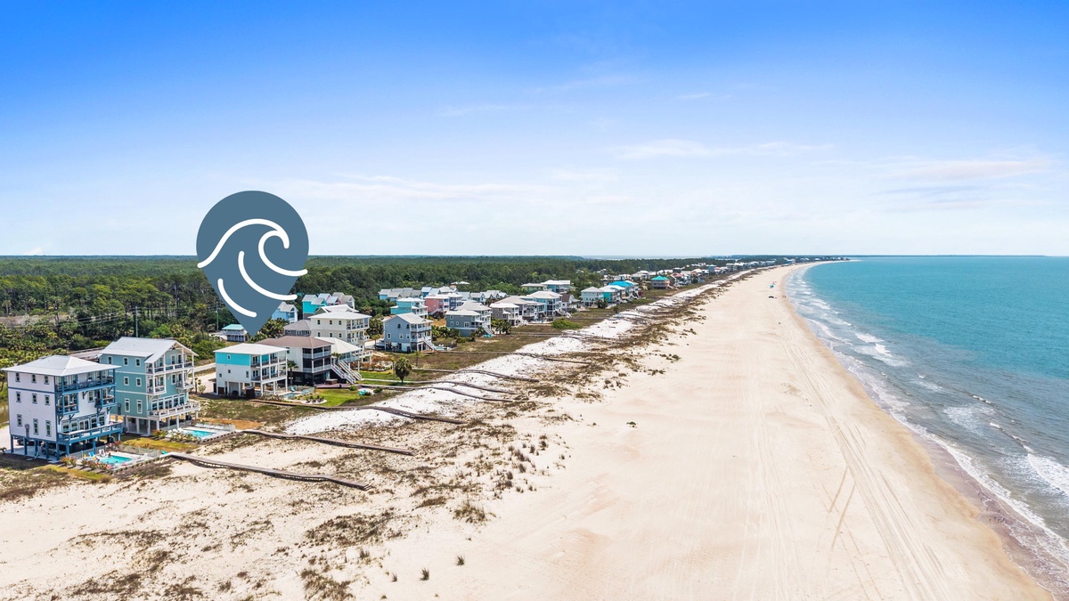 Aerial view of a pristine beachfront community nestled between lush coastal forests and turquoise waters, showing the property's prime location along this beautiful stretch of shoreline.