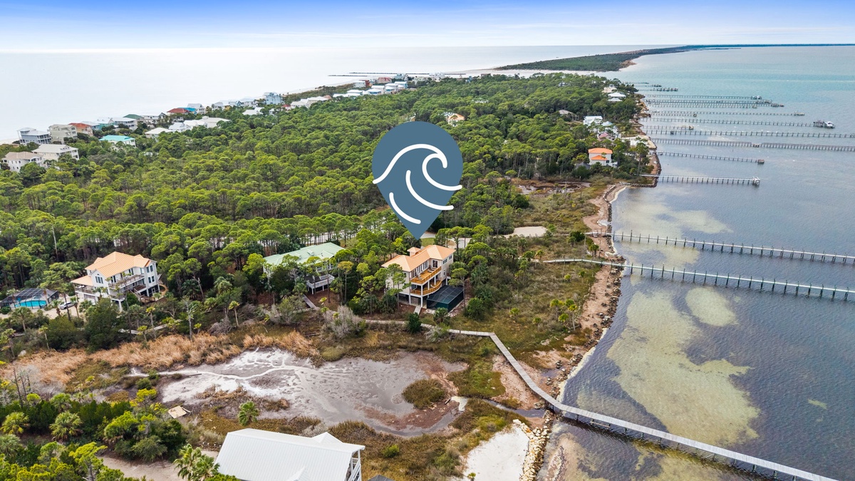 Stunning aerial view of waterfront properties nestled among lush vegetation with pristine bay waters and wooden pier structures extending into turquoise shallows.