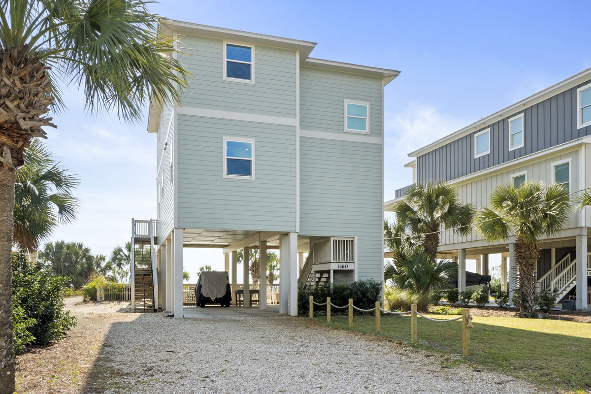 Charming coastal home elevated on stilts with tropical landscaping and covered parking beneath.