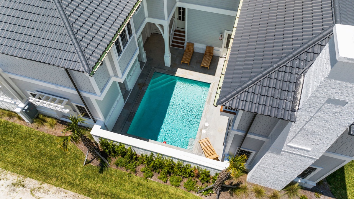 Aerial view of a private vacation rental home featuring a courtyard pool, lush landscaping, and tiled roofs with sunny outdoor relaxation areas.