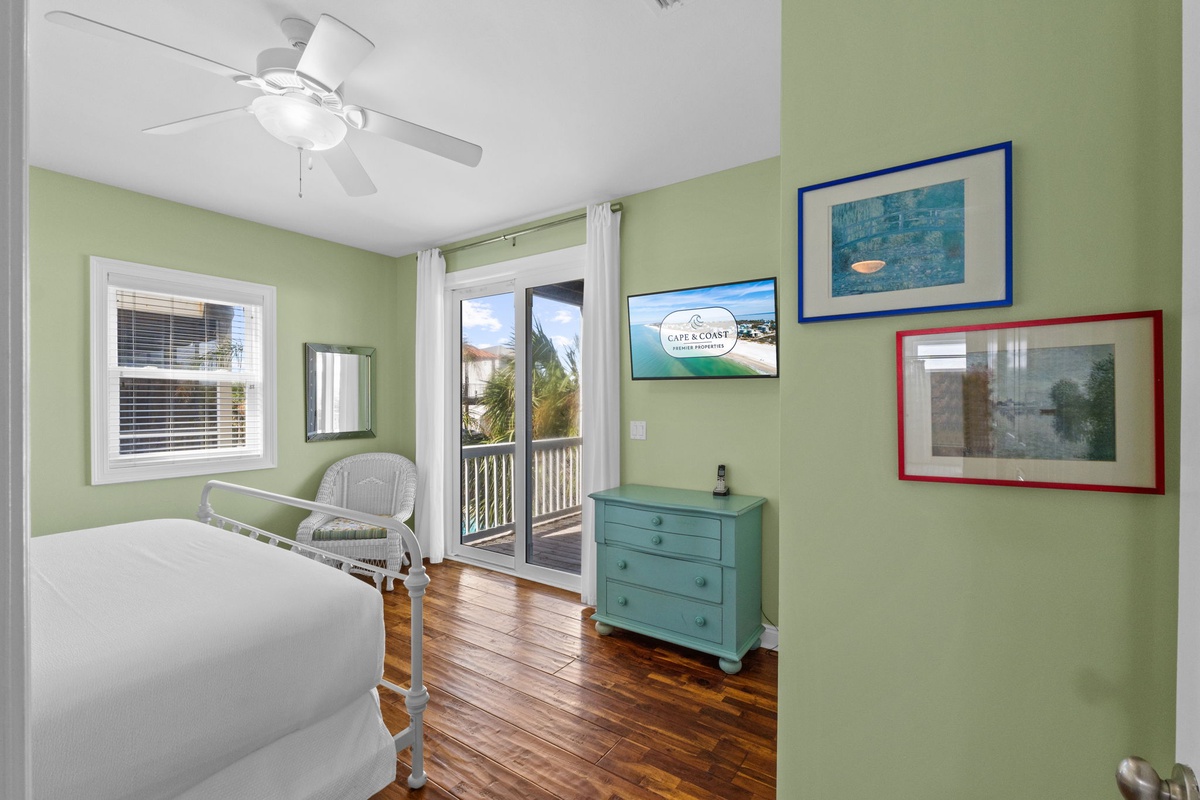 Your cheerful bedroom opens to a private balcony, inviting fresh sea breezes and soft natural light through glass doors. Gleaming hardwood floors and gentle green walls create a calm retreat after sunny beach days.