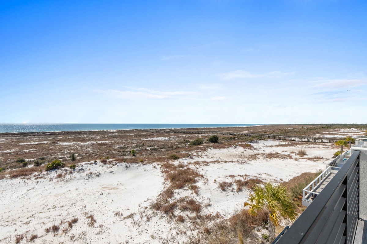 Coastal dunes and pristine beachfront stretch toward the horizon, with boardwalk access leading to the sandy shores.