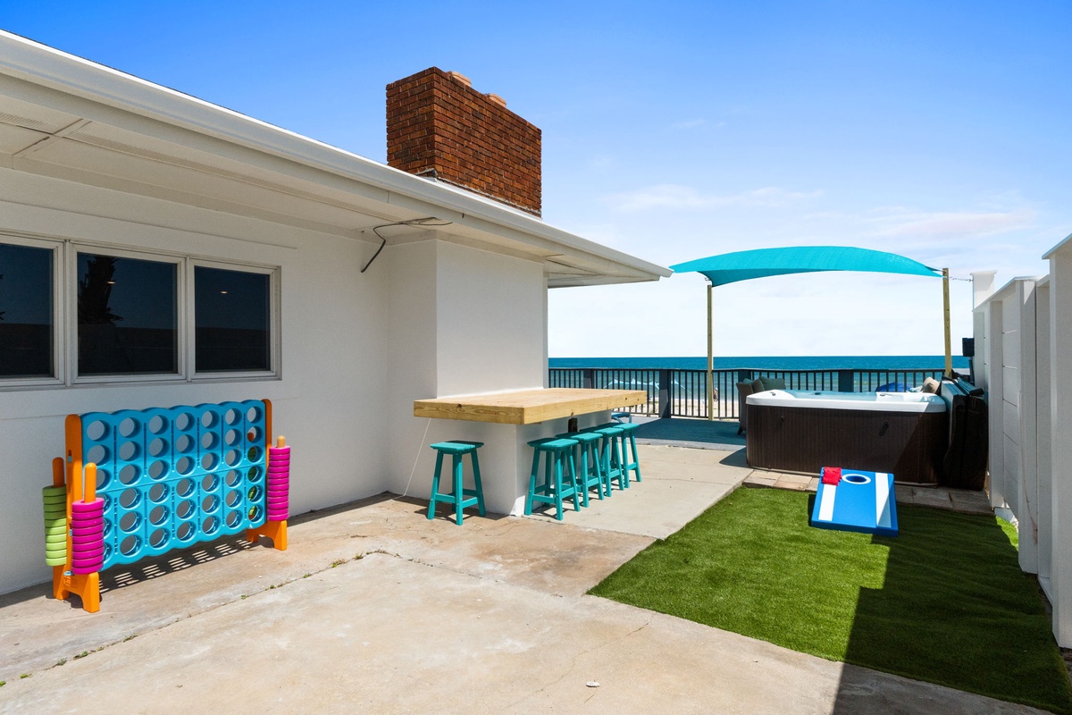 Your private outdoor space is ready for fun and relaxation, with a hot tub, shaded dining bar, colorful games, and a peaceful view beyond the railing.