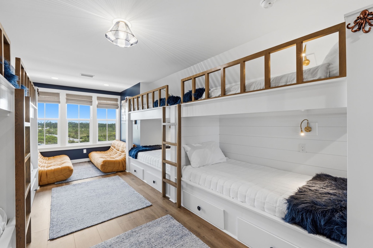 Your bunk room features custom built-in beds with plush bedding, warm wood accents, and golden loungers by the window. Natural light fills the space, creating a cozy retreat for restful sleep and relaxation.