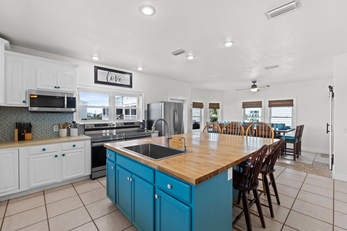 Your spacious open-plan kitchen invites you to cook and gather around the large island with butcher-block countertop, where bright windows and coastal-inspired teal accents create a welcoming, relaxed vibe.