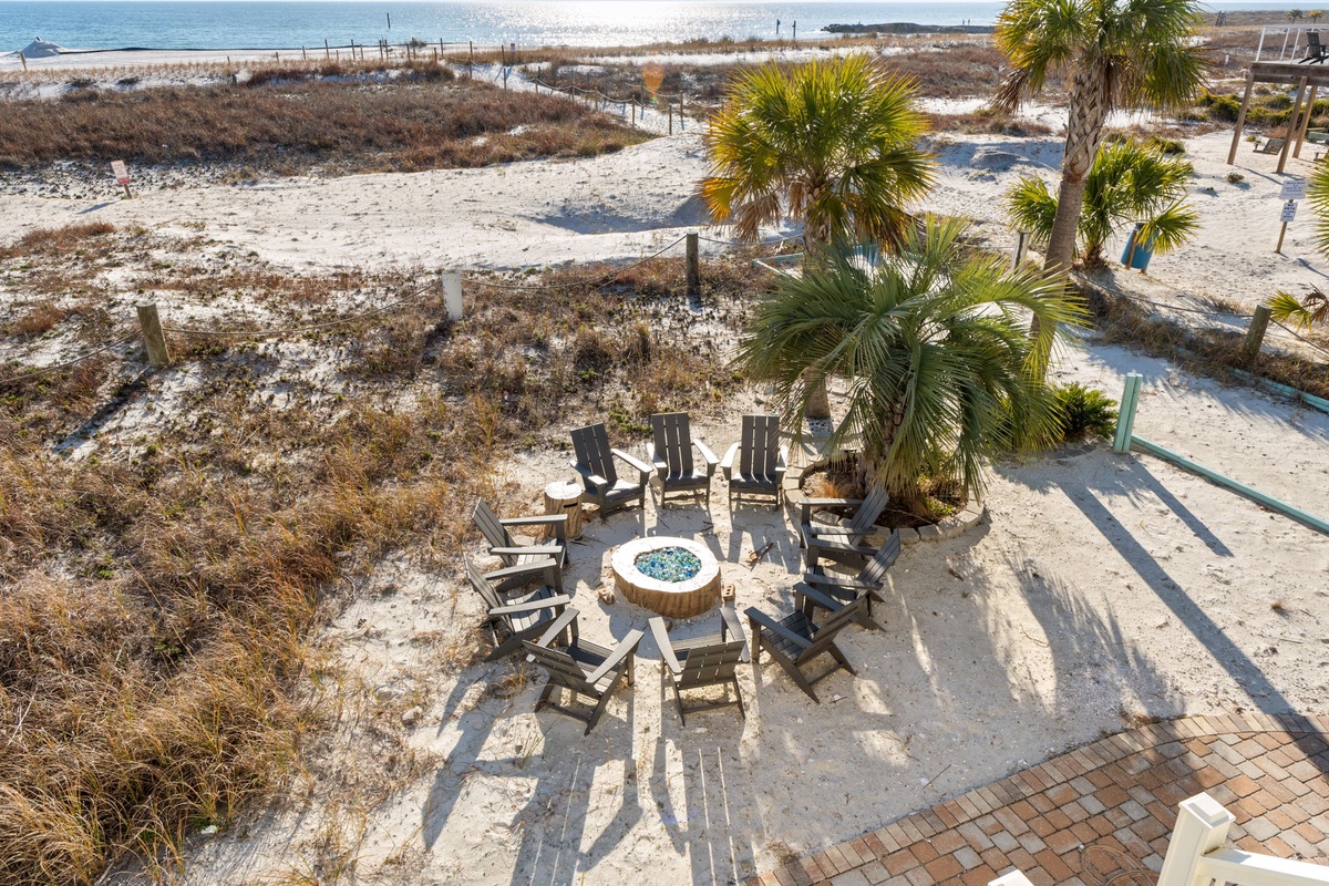 Beachfront fire pit area with Adirondack chairs surrounded by native palms and coastal dunes.