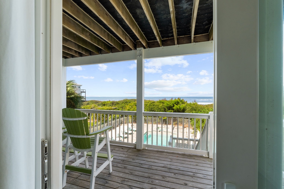 Step through your door to a covered balcony where coastal breezes meet sweeping ocean views. Two colorful chairs invite you to relax and watch the waves roll in, with lush greenery and sparkling pool below framing your perfect seaside retreat.