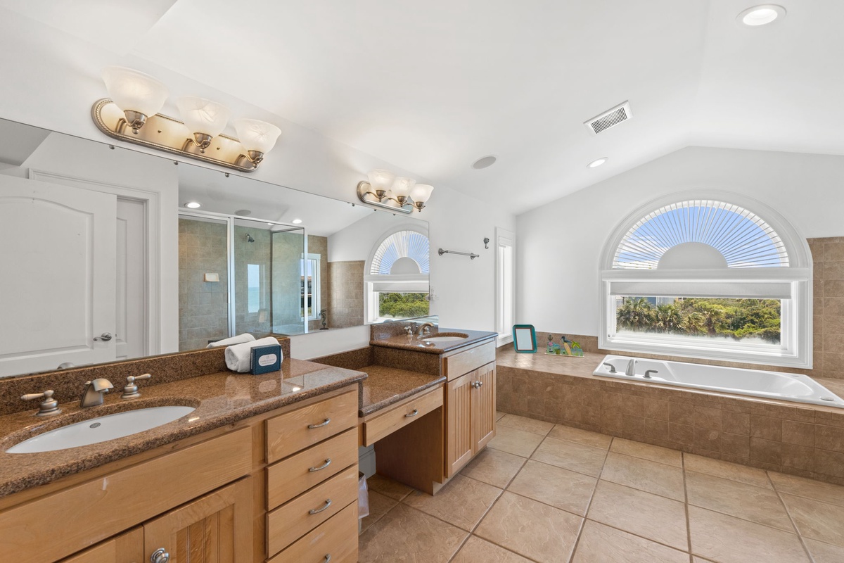 Indulge in your private spa-like bathroom with dual vanities, a soaking tub framed by elegant arched windows, and a spacious walk-in shower—your perfect retreat after a day of adventure.