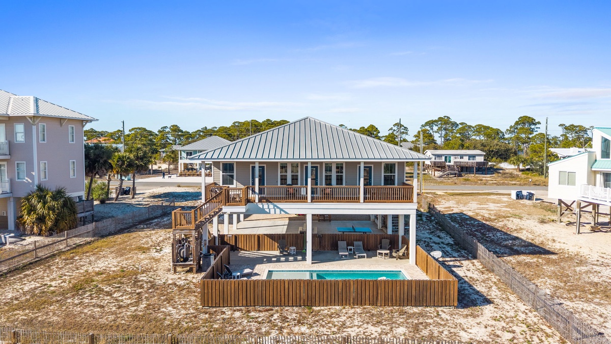 Stunning elevated beach house featuring a private pool, expansive deck, and coastal architecture surrounded by natural dunes and neighboring properties.