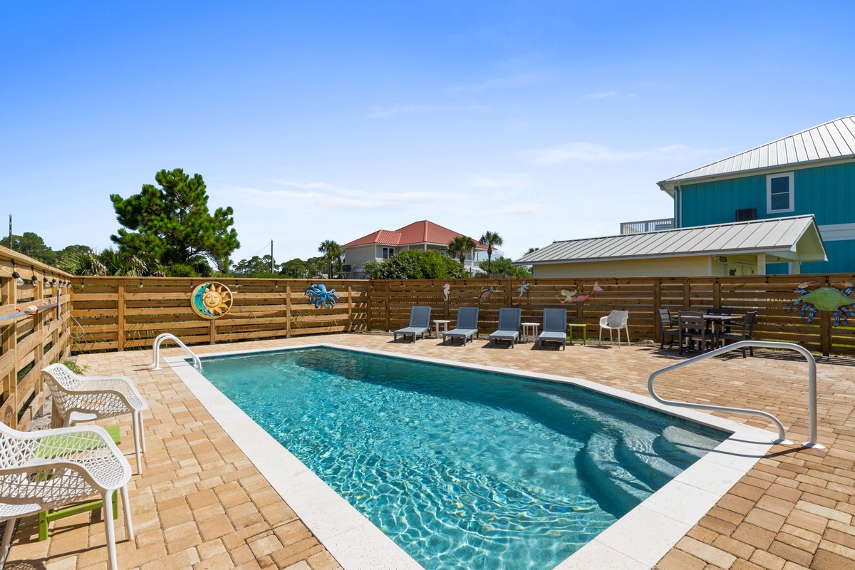 Your private pool awaits beneath clear blue skies, surrounded by loungers and cheerful coastal decor. This spacious outdoor oasis invites you to soak up the sunshine, cool off, and unwind in your own tranquil backyard retreat.