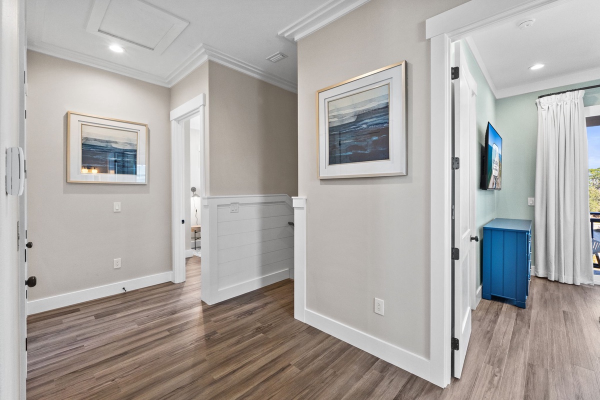 Step into your elegantly appointed hallway where coastal artwork and warm wood floors create a welcoming atmosphere throughout your vacation home.