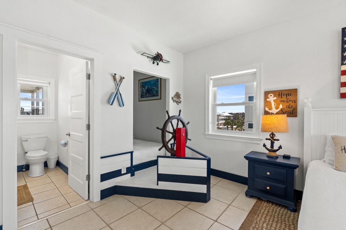 Your nautical-themed bedroom features charming navy and white accents, a cozy bed, and natural light streaming through windows that frame glimpses of the neighborhood beyond.