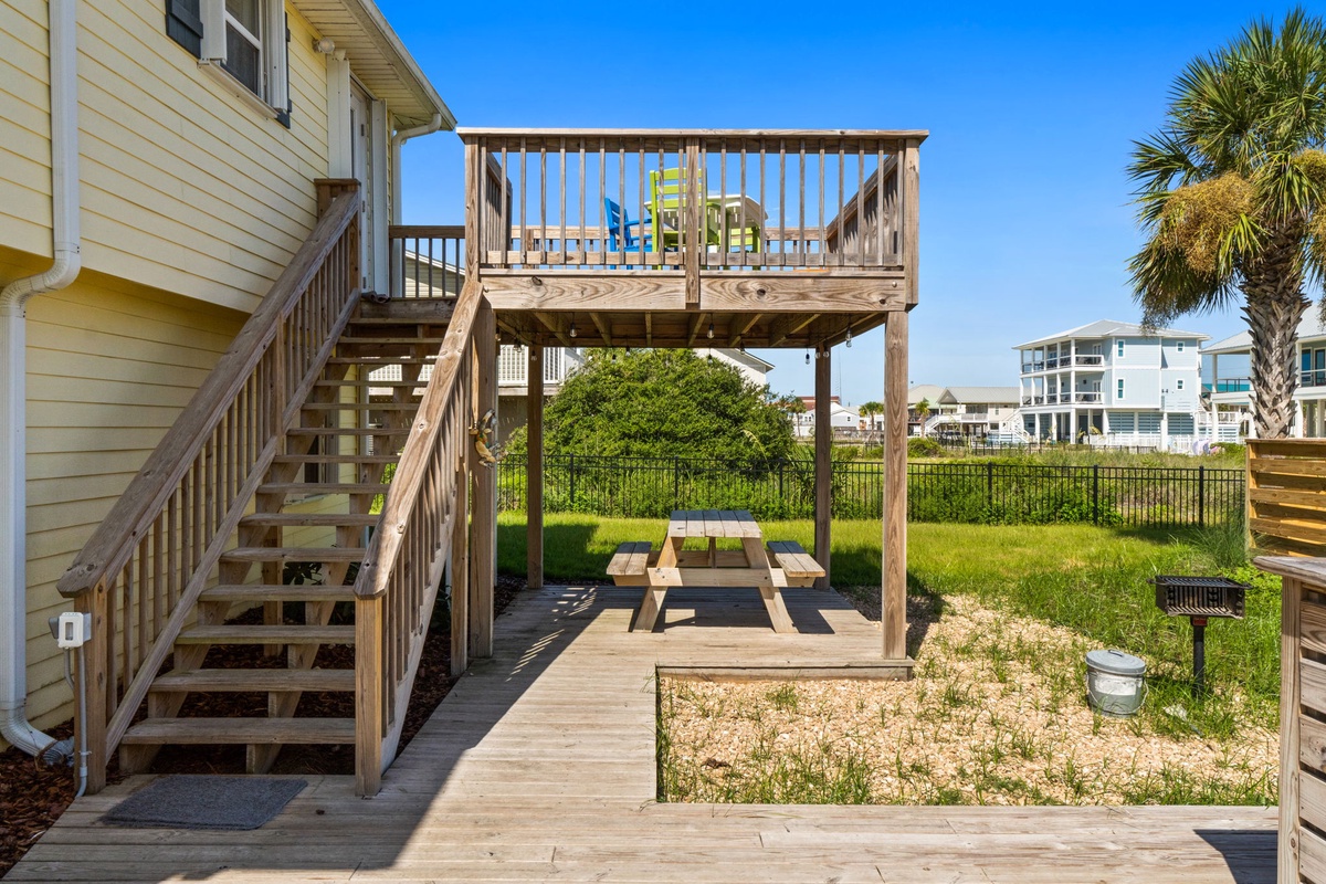 The property features a spacious backyard with elevated deck, covered picnic area, and lush green lawn—perfect for outdoor dining and relaxation under sunny coastal skies.