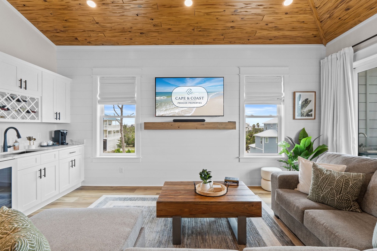 Your coastal retreat awaits with a bright open living space featuring vaulted wood ceilings, modern entertainment setup, and plush seating perfect for relaxing after beach adventures.