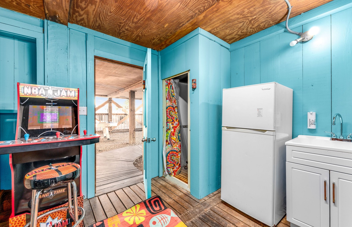 Your game room features vintage arcade entertainment and convenient kitchen amenities with vibrant turquoise walls and rustic wood ceiling.