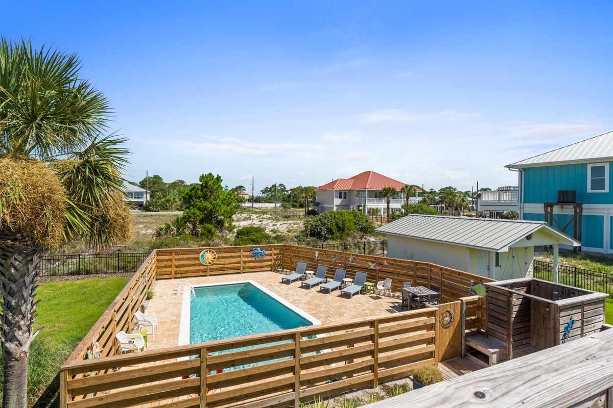 This coastal rental features a private pool, hot tub, and spacious deck with lounge chairs, all surrounded by palm trees and situated in a quiet beach neighborhood.